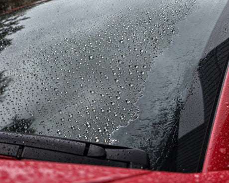 Anti-pluie à l'essai : les gouttes perlent sur le verre traité, un film d'eau reste sur le bord non traité