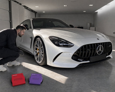 Daniel prüft im Streiflicht die Swirls auf der Motorhaube eines weißen Mercedes-AMG GT 63, davor Koch-Chemie Heavy Cut und Micro Cut Foam Pad auf dem Boden — gezeigt im Artikel „Polierpad-Farben verraten den Härtegrad nicht“